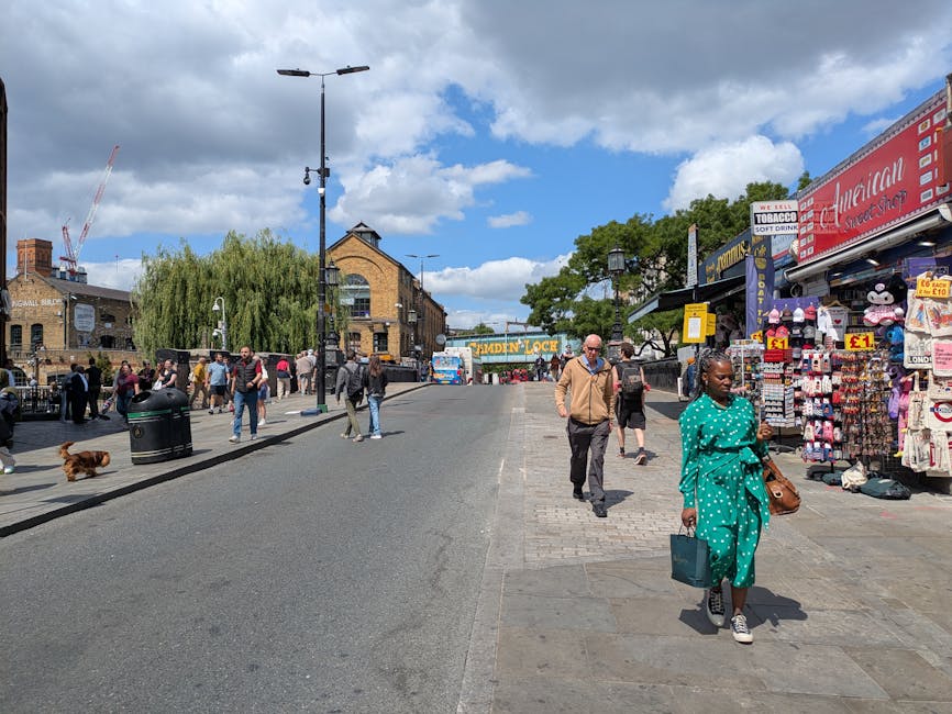 A busy street scene in Camden with a row of multi-story buildings, one featuring a large, colorful mural with graffiti-style artwork and text, including phrases like 'Graffiti for the People' and 'Lon
